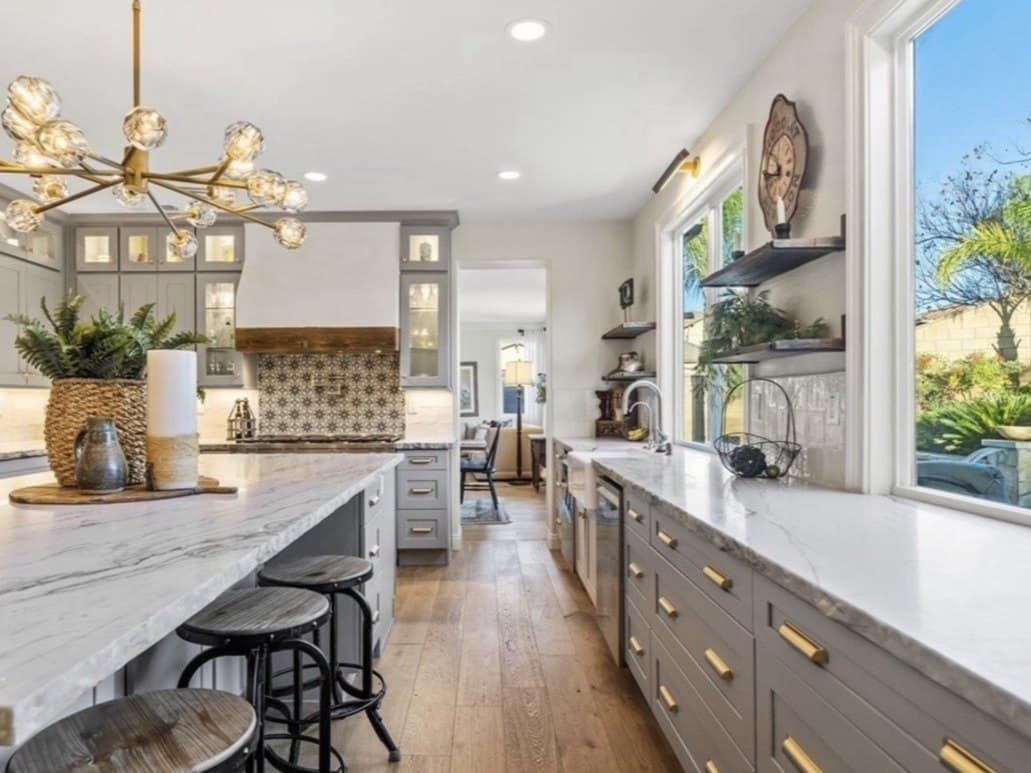 Remodeled kitchen concept: gray shaker cabinets, white quartzite counters, brass pulls and pendant, patterned tile behind the hood, wide-plank oak floor